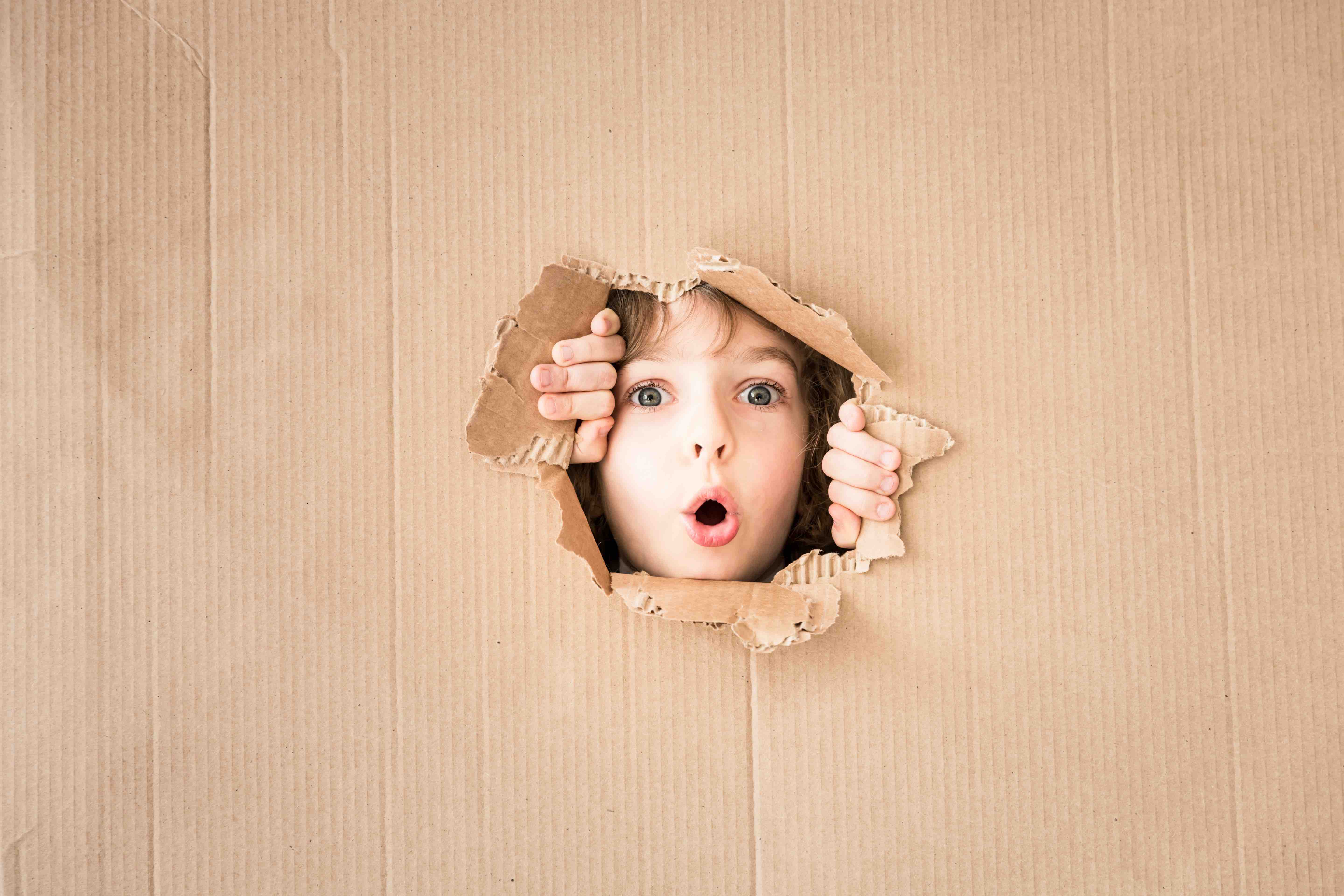 Portrait of surprised child looking through hole of cardboard. Copy space for your text